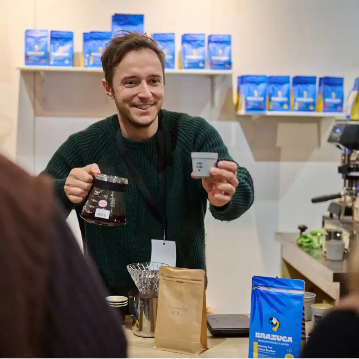 Smiling barista holding coffee and sample cup.